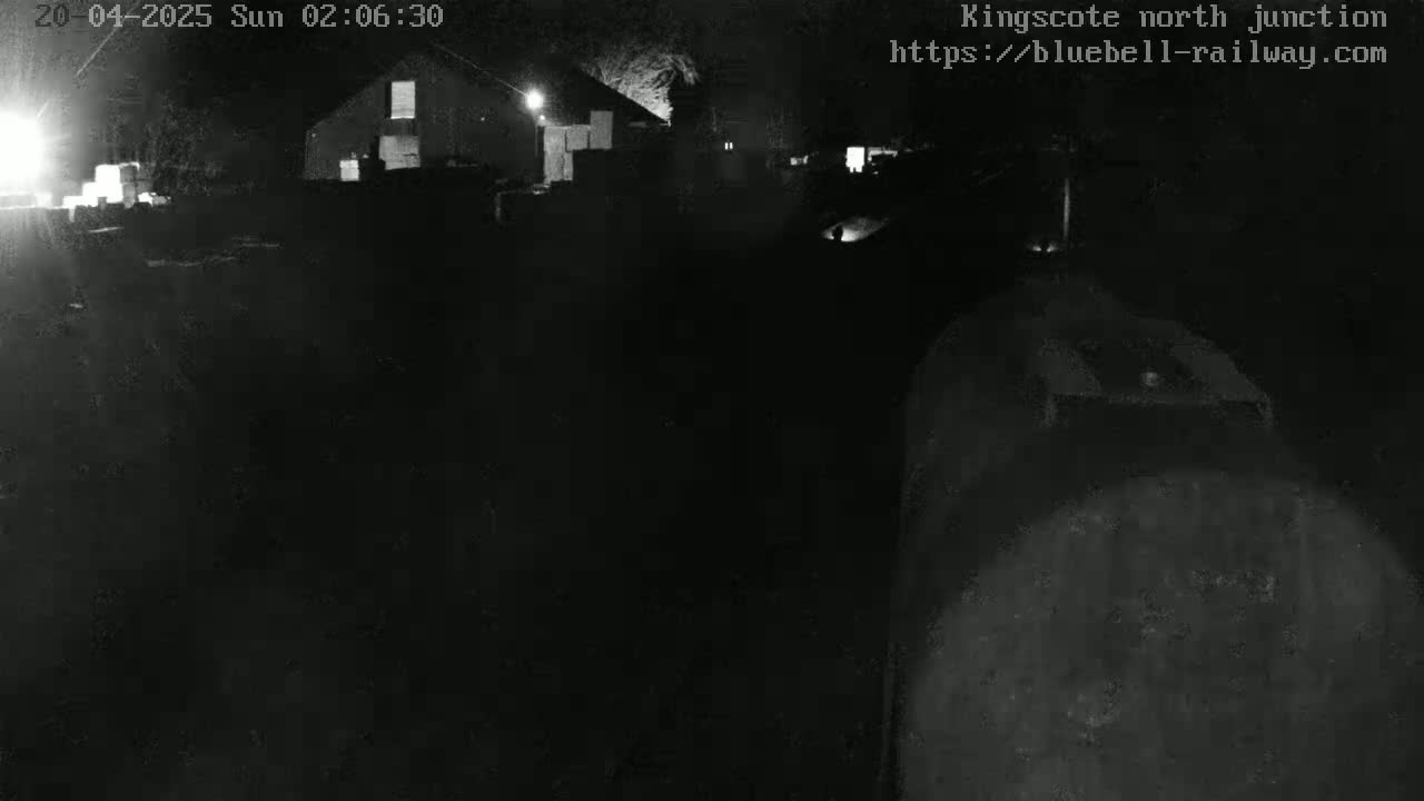 A nighttime, low-light view of a dark area with a building and some indistinct objects in the distance.