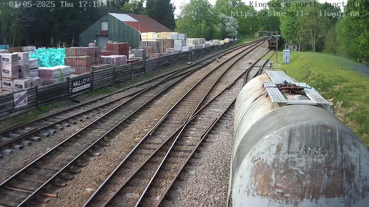 Railway tracks diverge past a building and stacks of building materials under a partly cloudy sky.