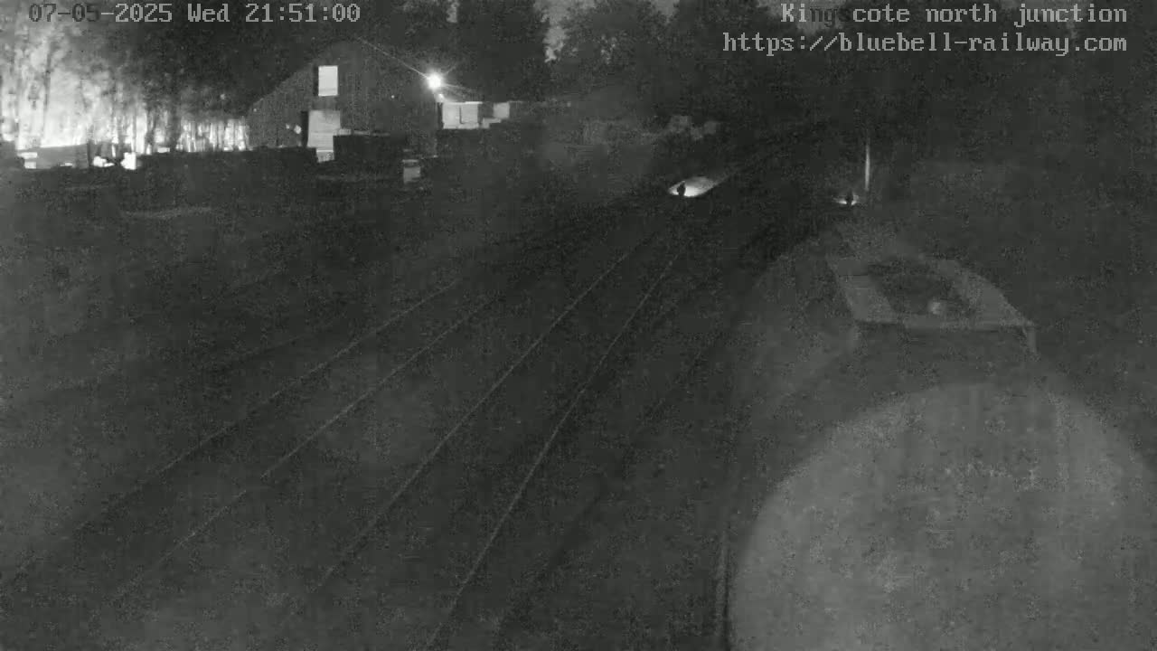 A nighttime, low-light view of train tracks leading to a building under a dark sky.