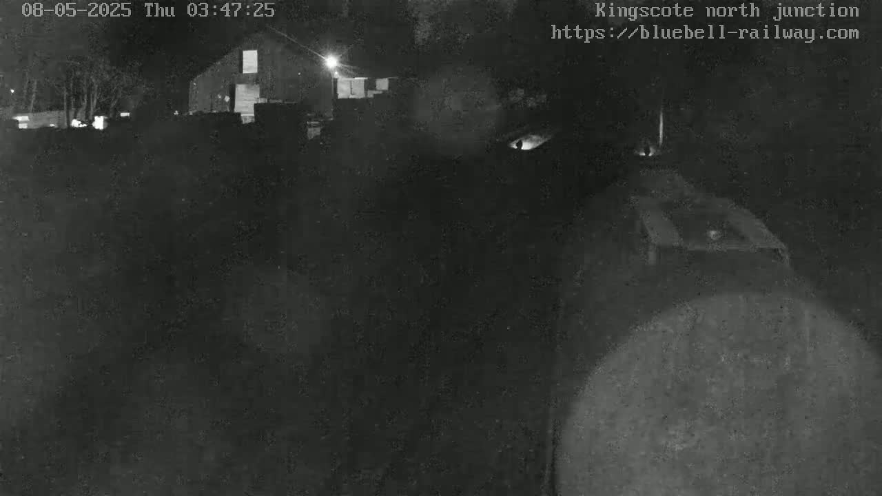 A nighttime, low-light image shows a dark, indistinct area with a building in the background.