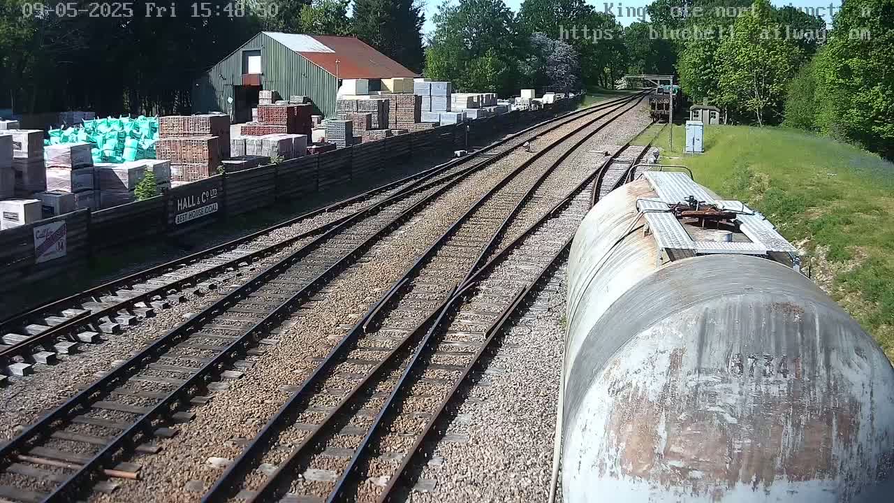 A view from a train car shows a railway junction, a building materials yard, and sunny weather.