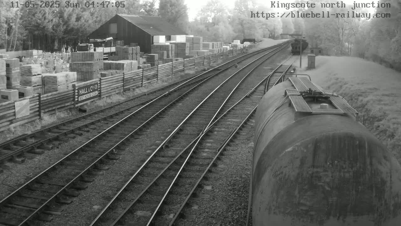 A view from a train shows a railway junction with multiple tracks, a building and stacked materials beside the tracks, and a hazy or foggy atmosphere.