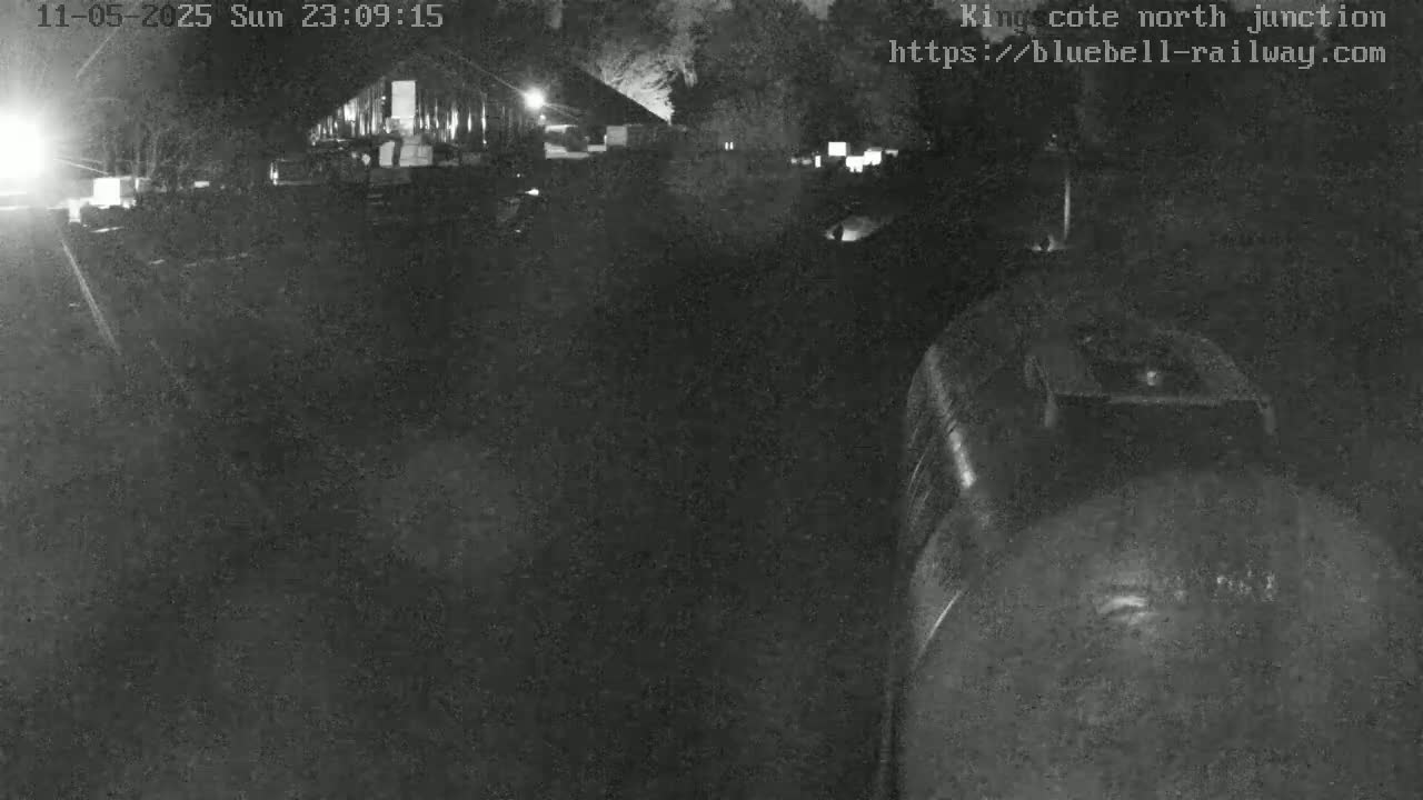 A nighttime, low-light view of a train approaching a dark, seemingly industrial area with a building in the background.