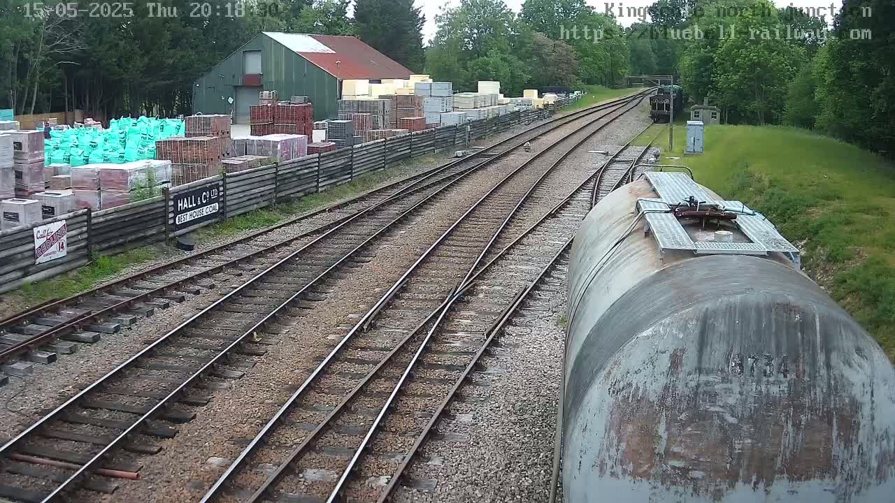 A railway track with a train car and stacks of building materials next to a building in a daylight setting.
