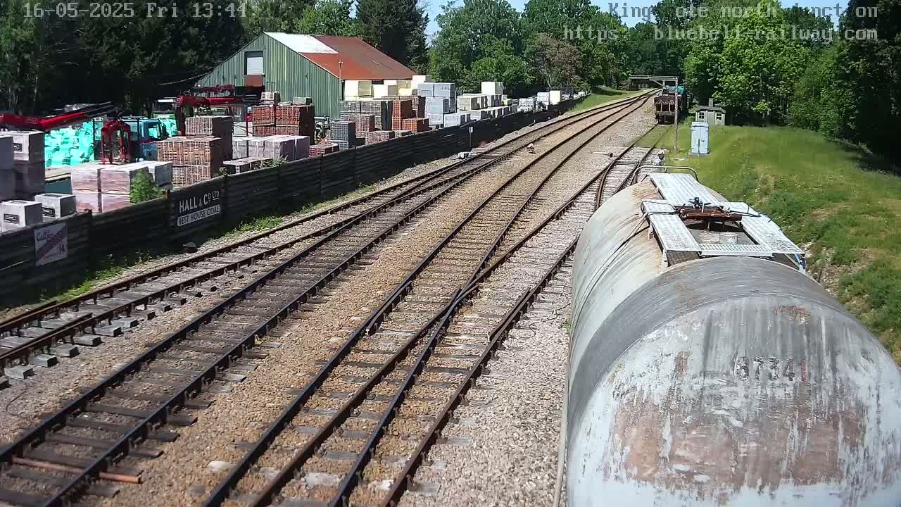 A view from a train shows multiple railway tracks branching off, alongside a building site with stacked building materials and a weathered train car.