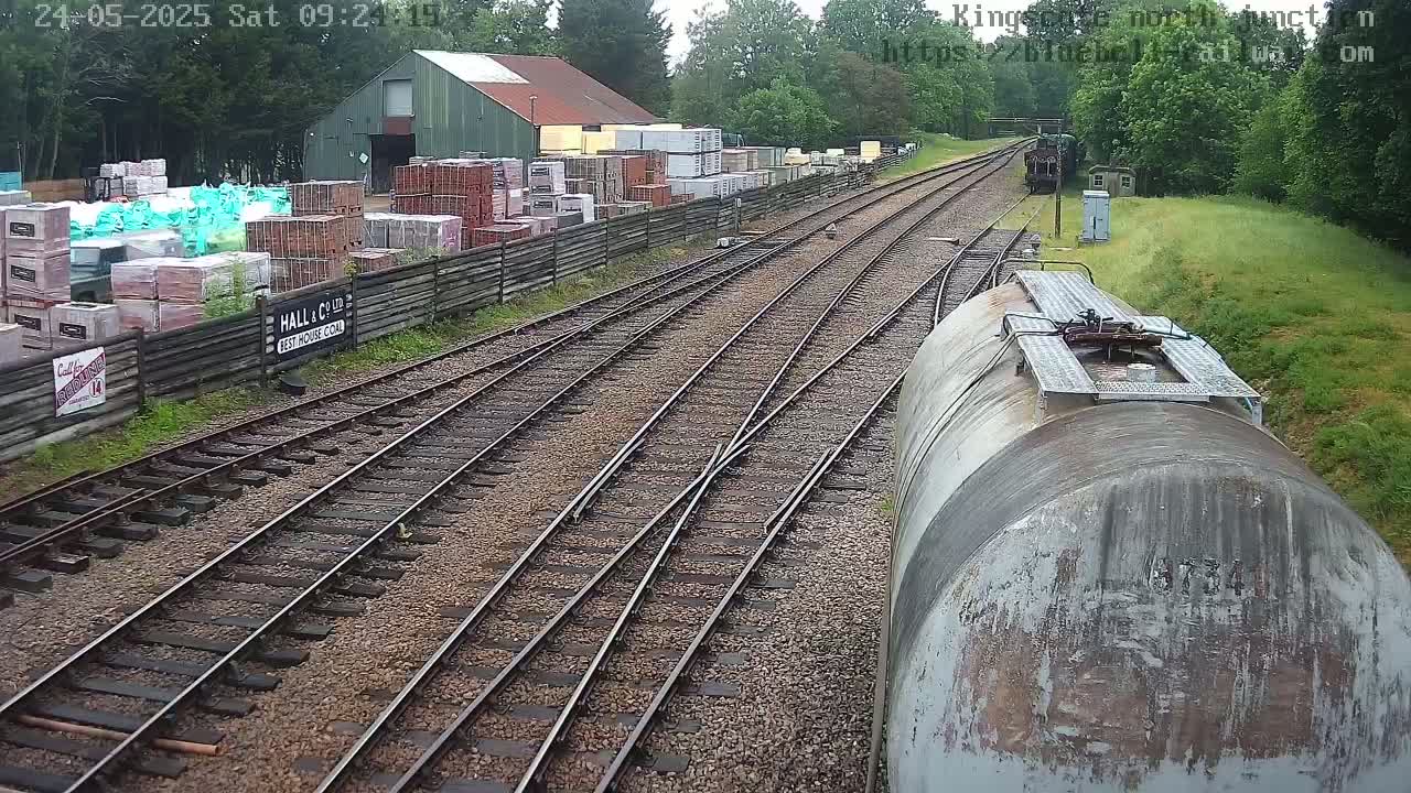 A railway switching yard on an overcast day with stacks of building materials beside it, and a train car in the foreground.