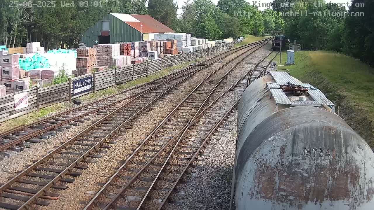 A train car moves along a railway track, passing a building yard filled with stacked bricks and other building materials under a partly sunny sky.