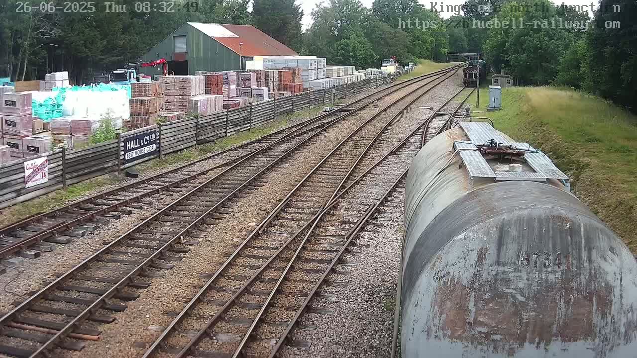 A view from a train of a railway line splitting into two, with a building and stacks of building materials to one side, under a partly sunny sky.