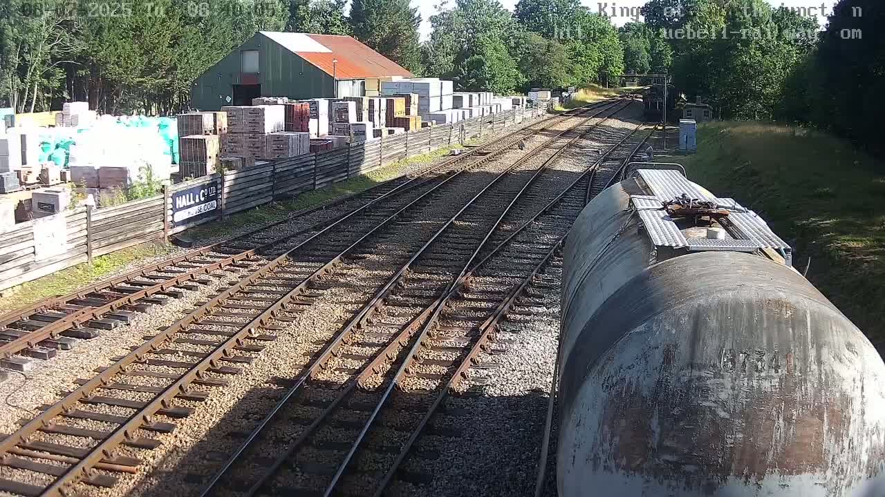 A train travels past a building materials yard on a sunny day, alongside multiple railway tracks.