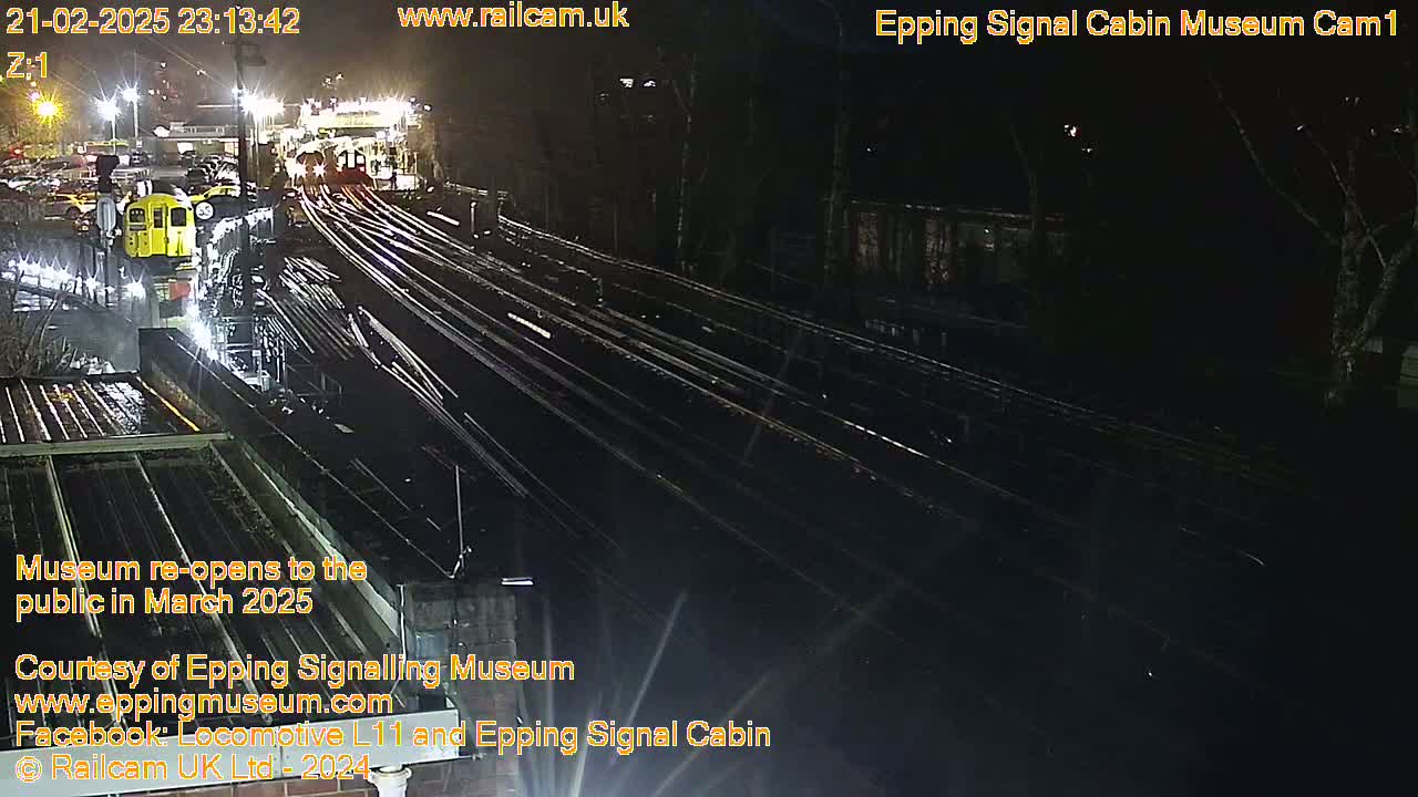 A nighttime, overhead view of a train station with multiple train tracks and a yellow train visible near a building.