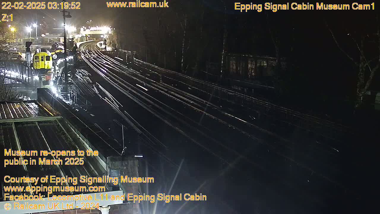 A nighttime, overhead view of a train yard with a yellow train and numerous train tracks.