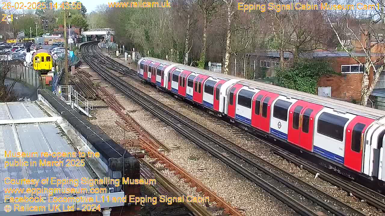 A red and white train is stopped on a railway track next to a yellow train, under a mostly clear sky.