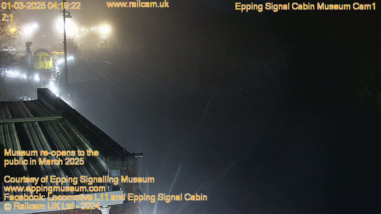 A train is visible in the foggy distance, near a building's roof at night.