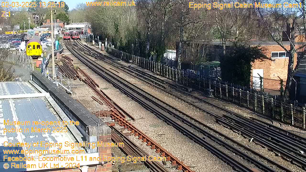 A sunny day at a train yard shows multiple railway tracks with several train cars visible, some parked and some moving.