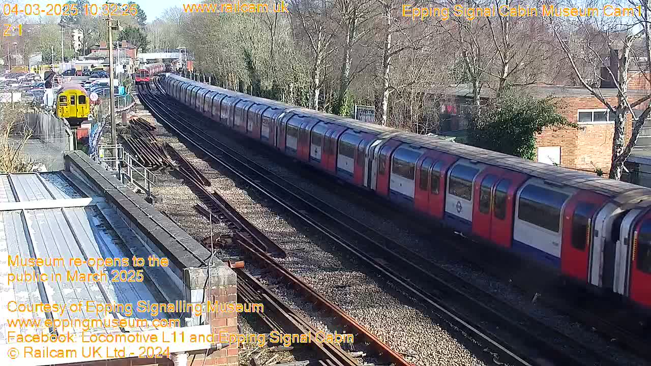 A long red and white train travels along train tracks on a sunny day, passing a smaller yellow train.