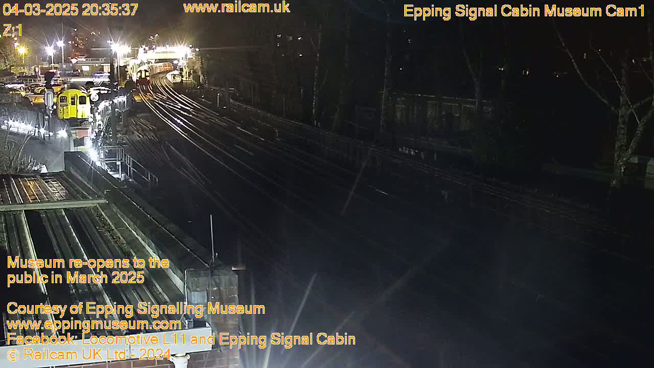 At night, a yellow train is parked near a rail yard with multiple tracks under bright lights.