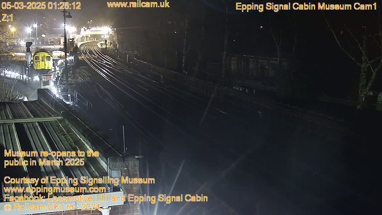 A nighttime, overhead view of a train station with a train visible on the tracks and surrounding infrastructure illuminated by artificial light.