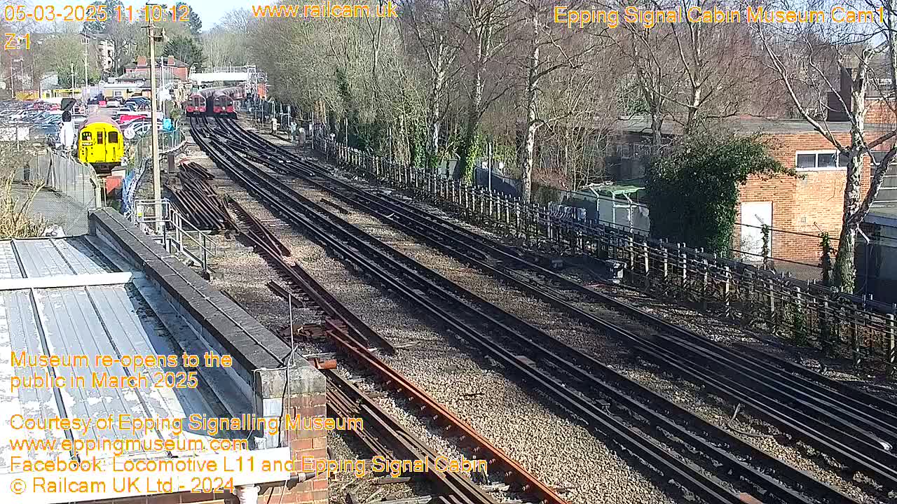 A sunny day reveals a high-angle view of multiple train tracks branching out from a railway station, with several train cars visible in the distance.