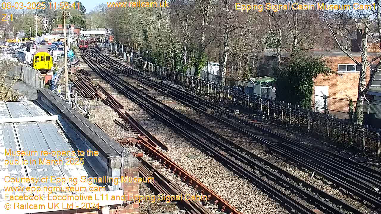 A sunny day view of a railway yard with multiple train tracks, a yellow train, and bare trees surrounding the area.