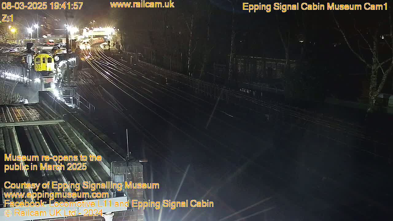 A nighttime view of a train yard with a single train car visible and several sets of train tracks under artificial lighting.