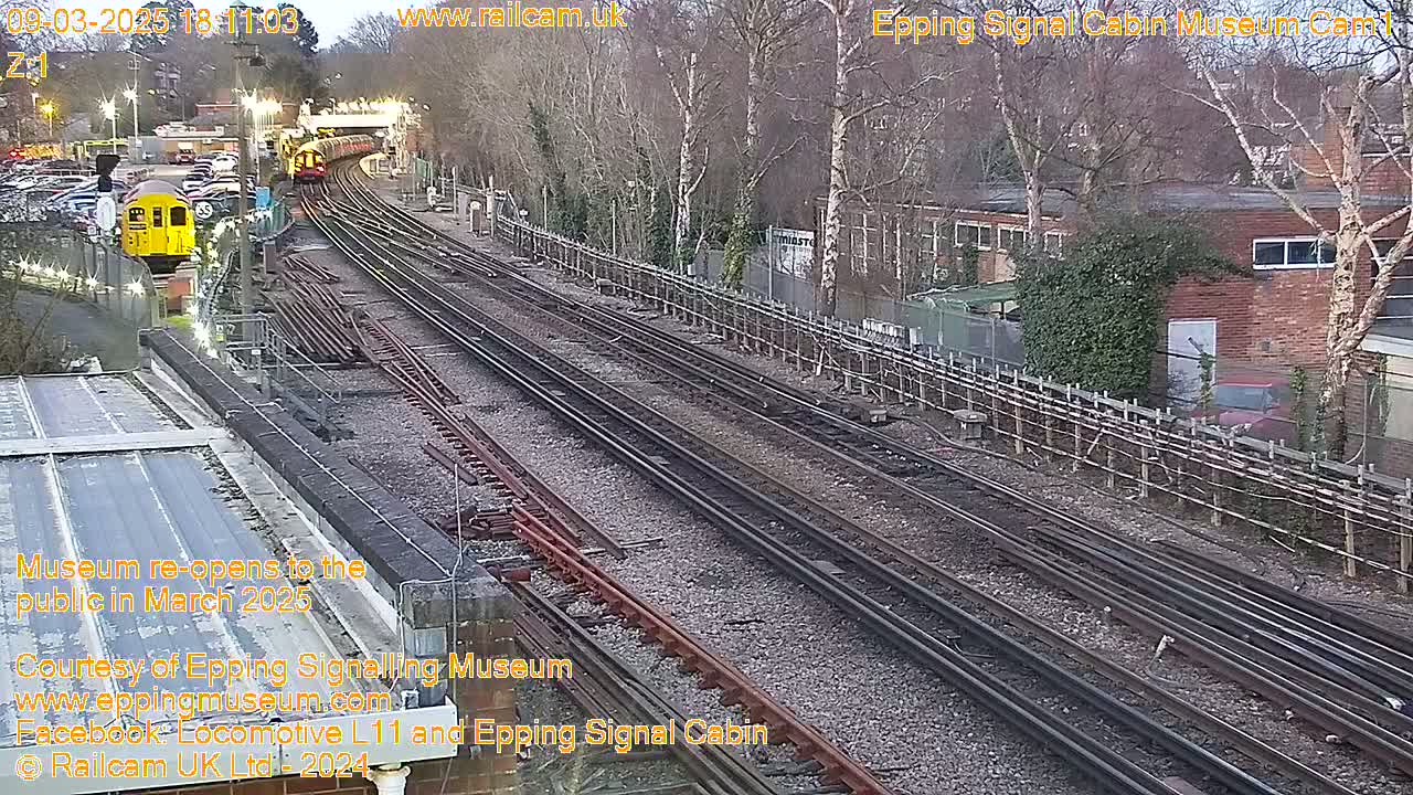 A high-angle, long shot of several train tracks and a railway station on an overcast day, with a yellow train visible in the distance.