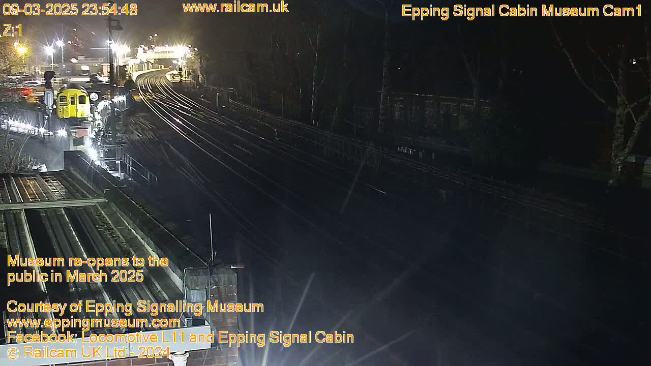 A nighttime view of a train station with a yellow train visible and multiple train tracks extending into the darkness.