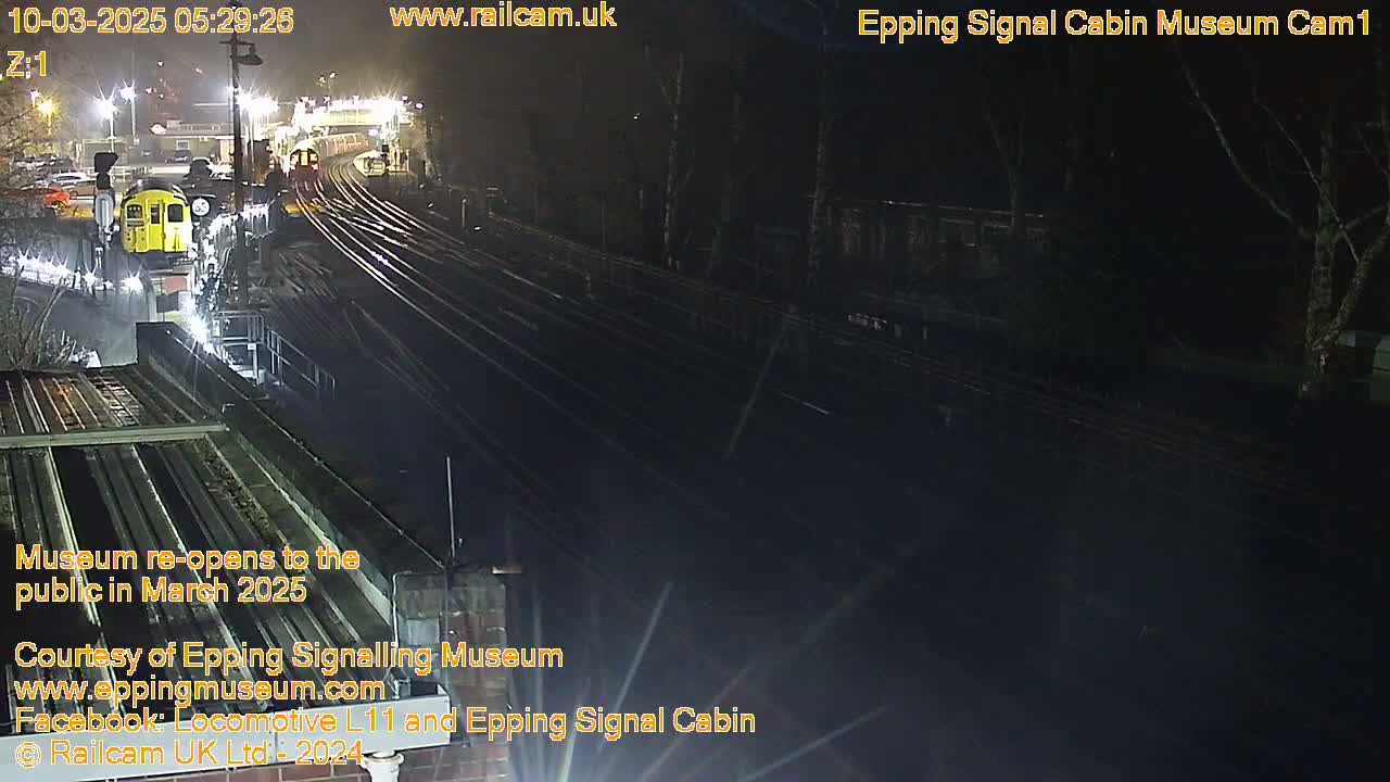 A nighttime, overhead view of a railway station with a yellow train and multiple sets of tracks.