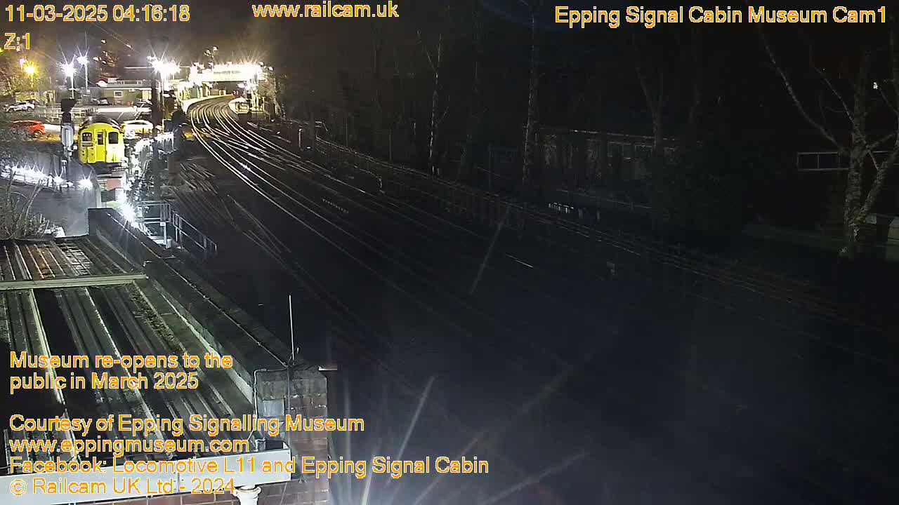 A nighttime, overhead view of a train station with a railway line and a single train car visible under artificial light.