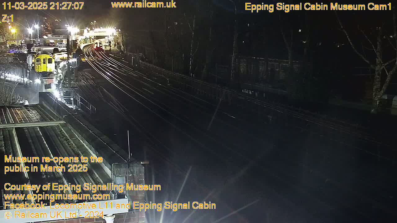 A nighttime view of a train station with a yellow train car and several sets of train tracks.