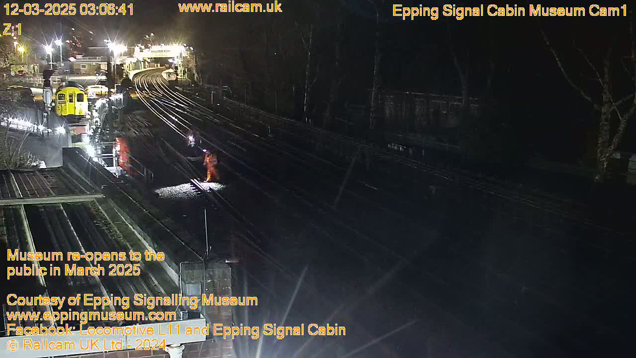 A nighttime view of a railway station with multiple tracks, some railway workers, and a train.