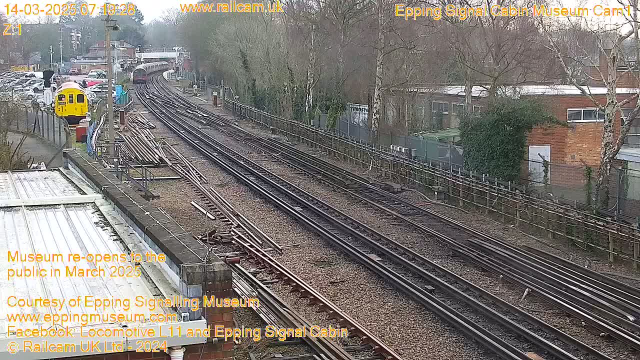 A railway station with multiple train tracks, a yellow train, and a building, on an overcast day.