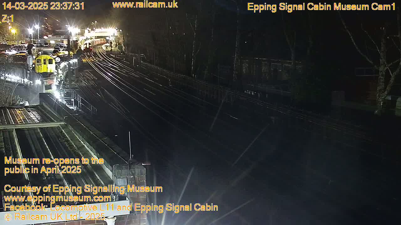 A nighttime view of a train station with multiple train tracks and a yellow train parked at a platform under artificial lighting.