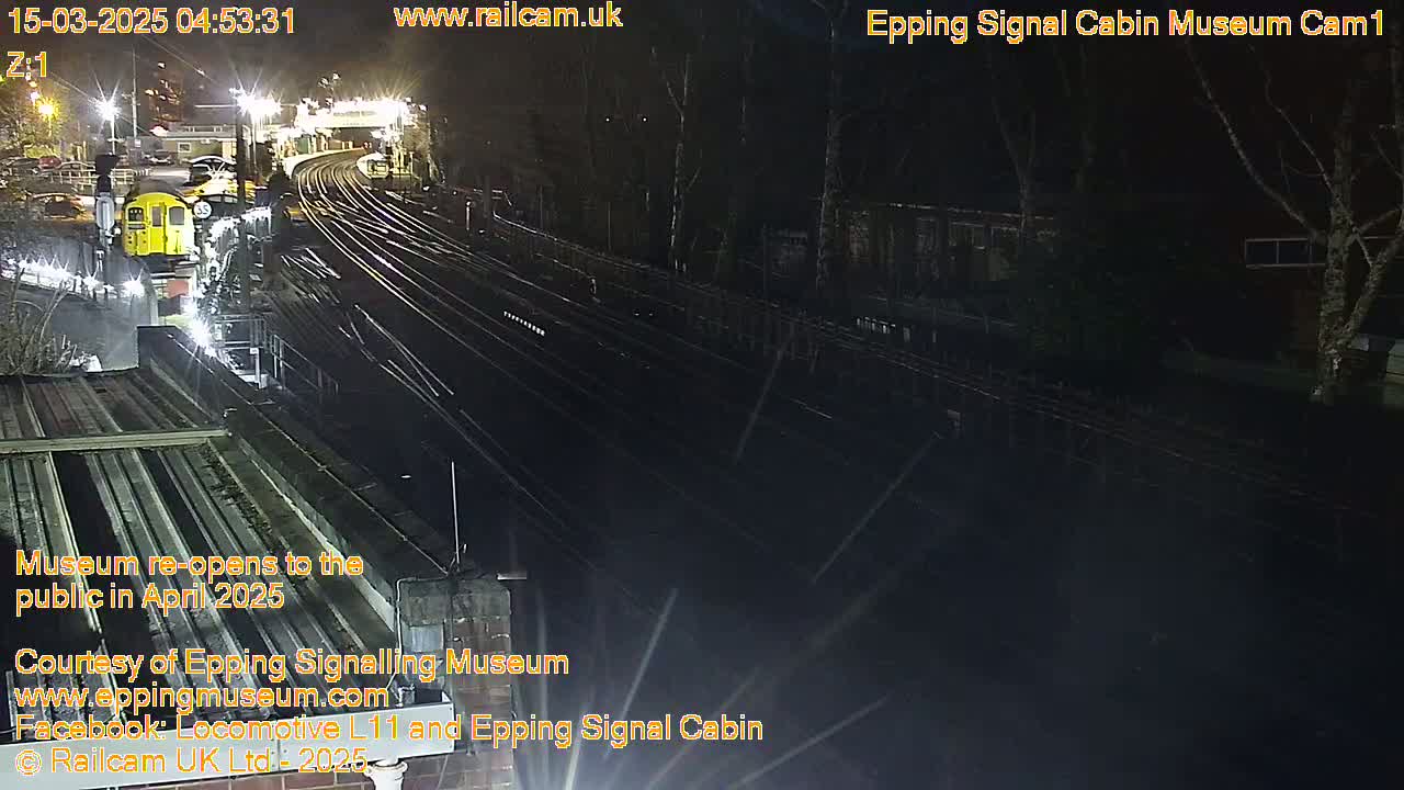 A nighttime, overhead view of a train station with a train stopped on the tracks, under partly cloudy skies.