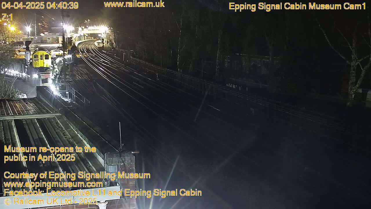 A nighttime view of a train station with a yellow train and multiple train tracks under artificial light.