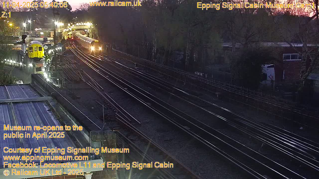 A twilight view of multiple train tracks with a train passing by, near a building surrounded by trees.