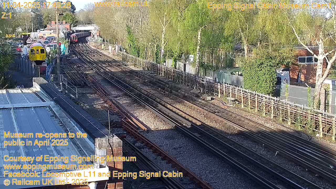A high-angle, sunny view of a railway station with multiple train tracks, a yellow train, and trees.