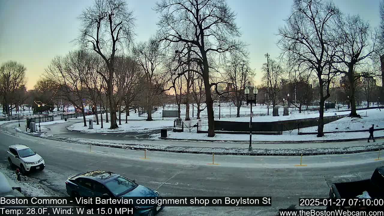 A snow-covered park with bare trees is visible from a street with cars parked on the side, under a twilight sky with a westerly wind.