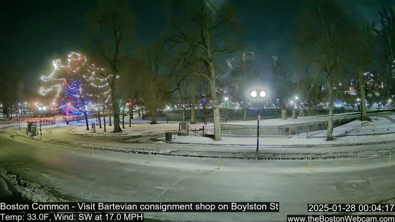 A snow-covered park at night, illuminated by streetlights and Christmas lights decorating trees, with a southwest wind at 17 mph and a temperature of 33°F.