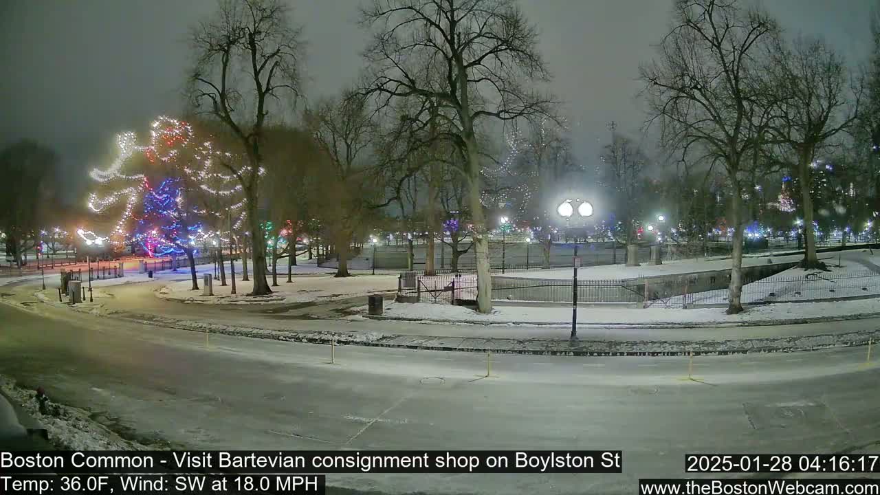 A snow-covered park at night, illuminated by holiday lights and streetlights, with a windy, 36°F temperature.