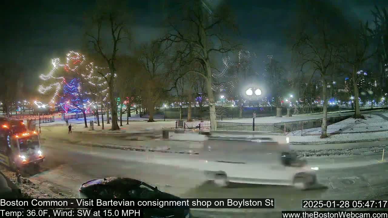 A snow-covered park at night features a large light display shaped like a person, with vehicles driving on a nearby road under a southwest wind of 15 mph and a temperature of 36°F.