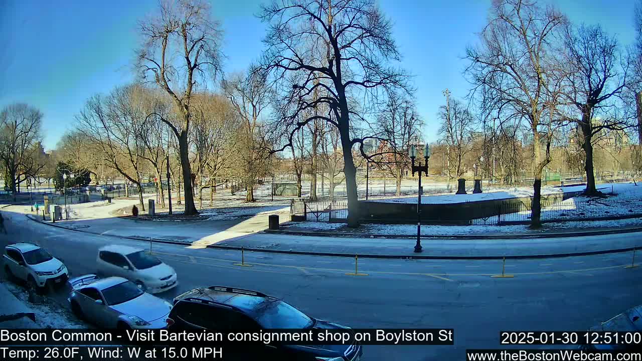 A sunny, snowy scene shows a park with bare trees and a street with several cars parked and driving, with a temperature of 26 degrees Fahrenheit and a 15 mph westerly wind.