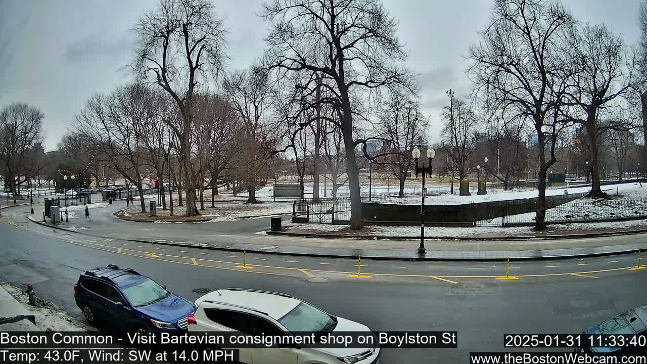 A partly cloudy, cool day with a southwest wind shows a view of a park with bare trees, a road curving through it, and two cars parked along the side.