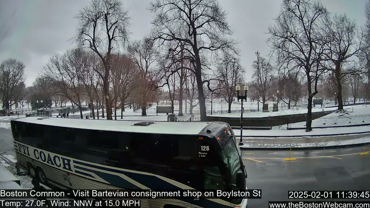 A large tour bus is parked on a snow-covered street next to a park with bare trees under an overcast sky.