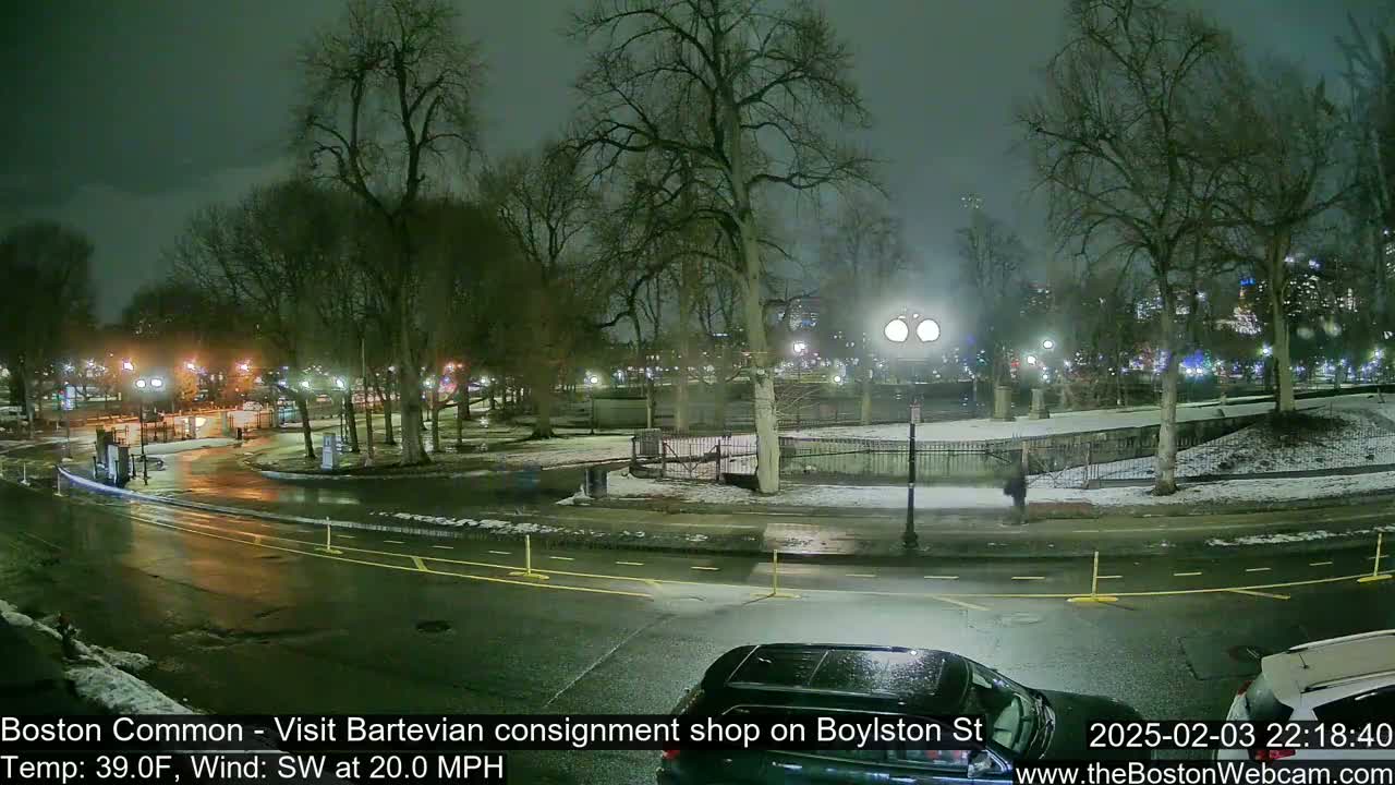 A nighttime view of a park with snow on the ground and wet roads, under a dark, overcast sky, with a southwest wind at 20 mph.