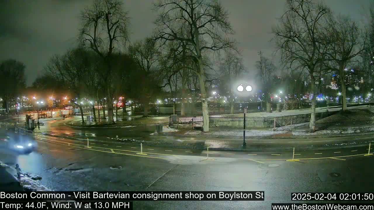 A nighttime view of a park with wet roads and a few cars, under cloudy skies with a 13 mph westerly wind.