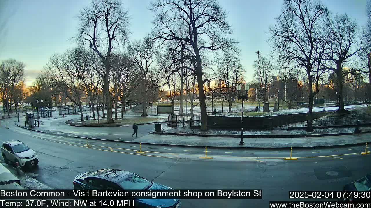 A mostly clear, cool morning reveals a park with bare trees, a few pedestrians, and cars on a road next to it.