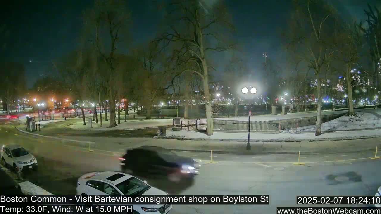 A nighttime scene shows a snow-covered park with cars driving on a road, under a dark sky with a temperature of 33°F and a 15 mph west wind.