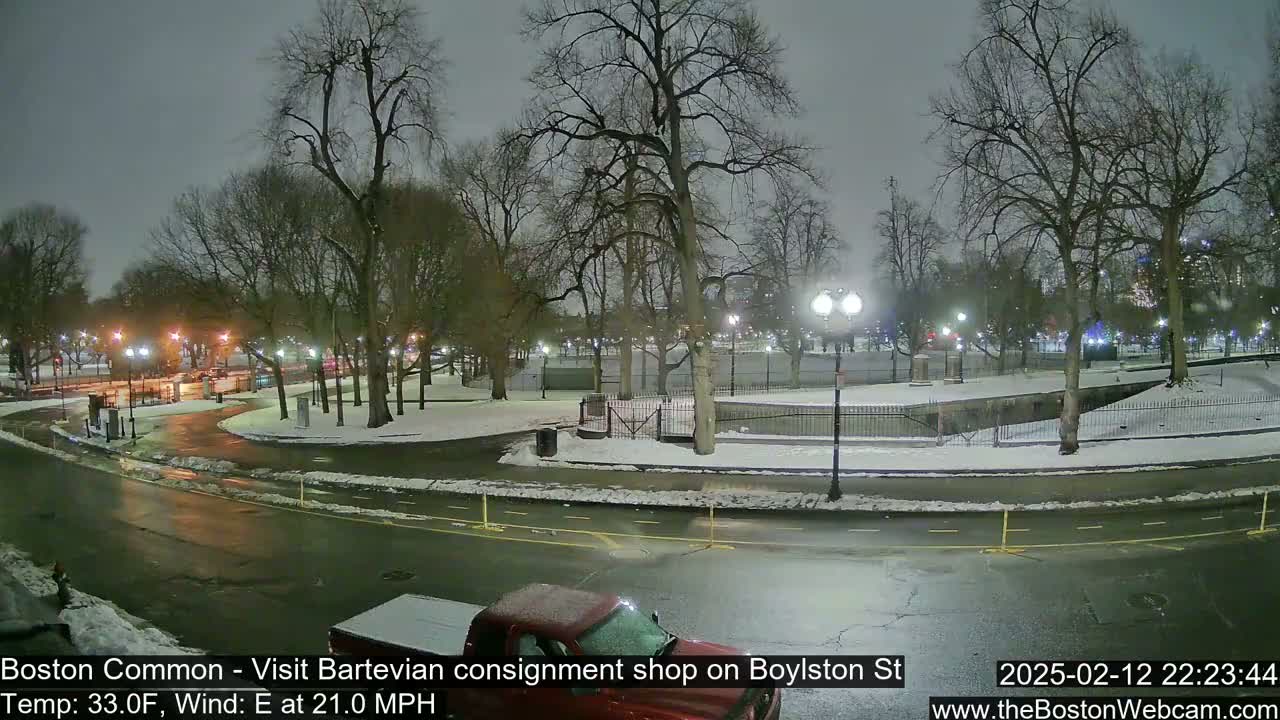 A nighttime view of a snow-covered park with a road curving through it, under a cloudy sky with a chilly temperature and strong easterly wind.