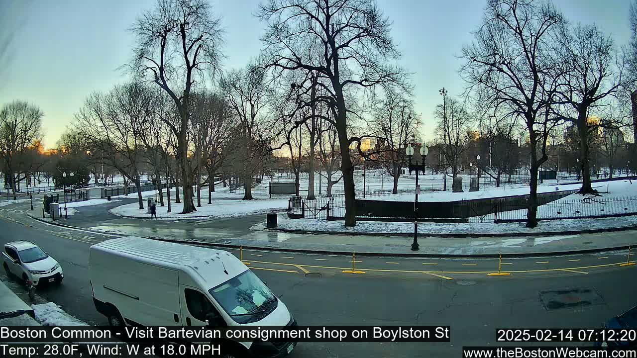 A snow-covered park with bare trees is visible from a city street where two vehicles are parked, under a partly clear sky at sunrise.