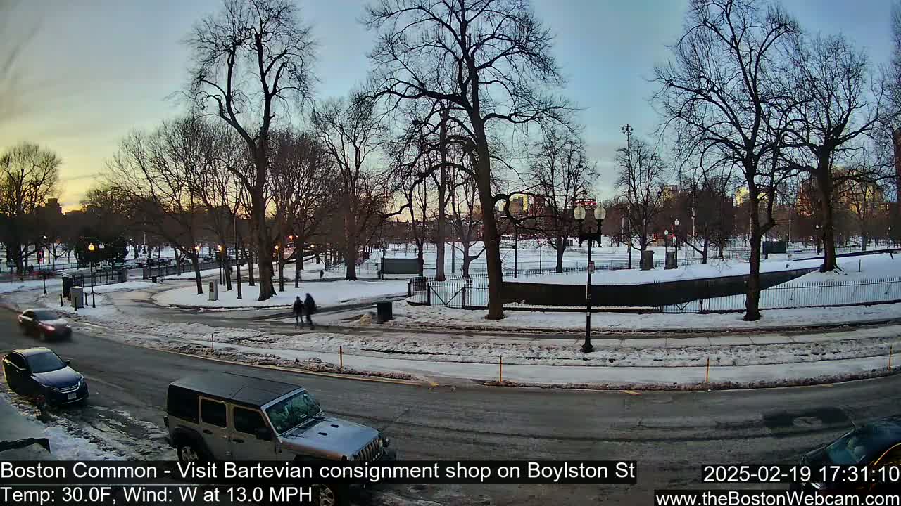A snow-covered park with bare trees and a road with cars is visible during a twilight hour with a temperature of 30°F and a westerly wind of 13 mph.